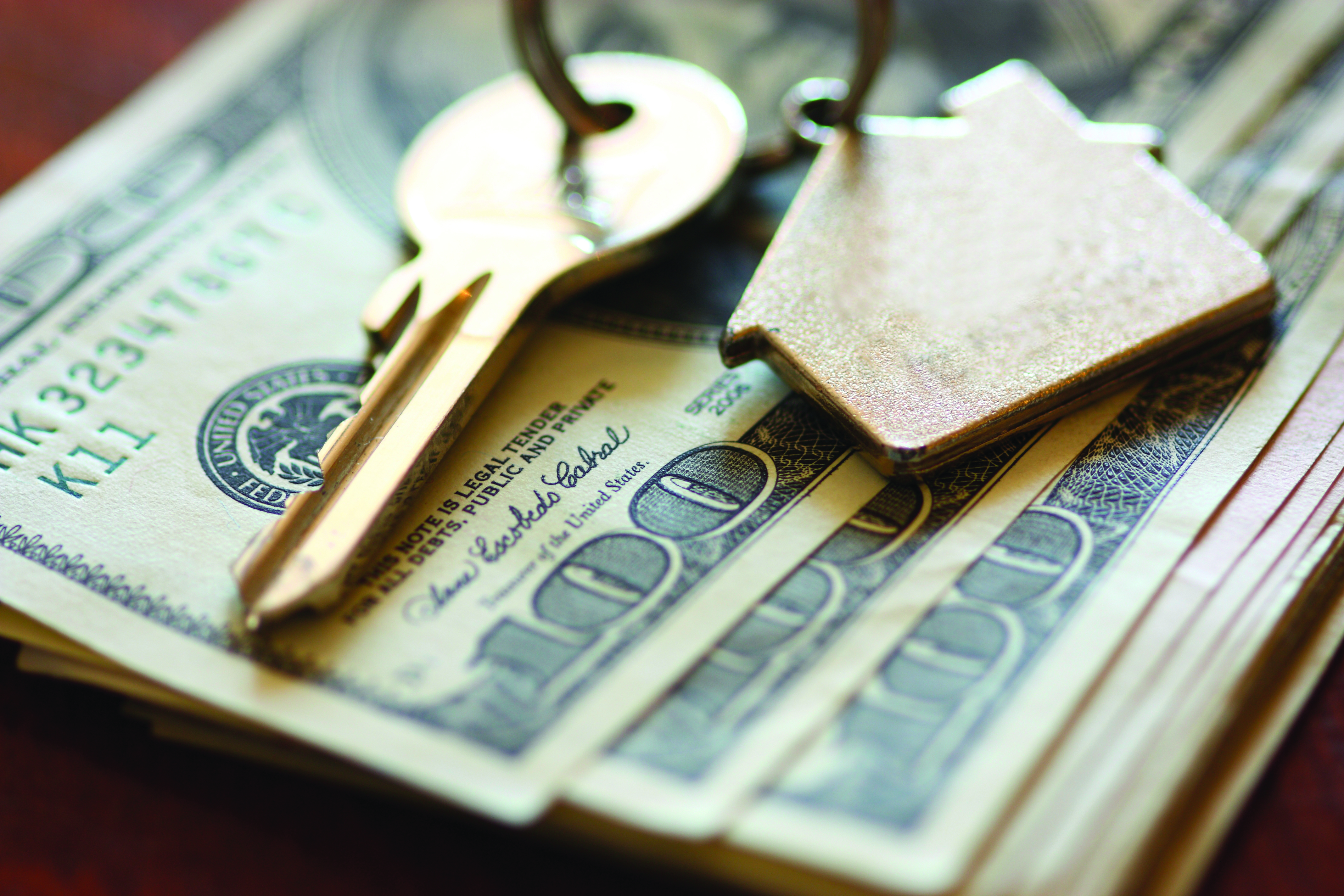 money fanned out with gold house key and house keychain