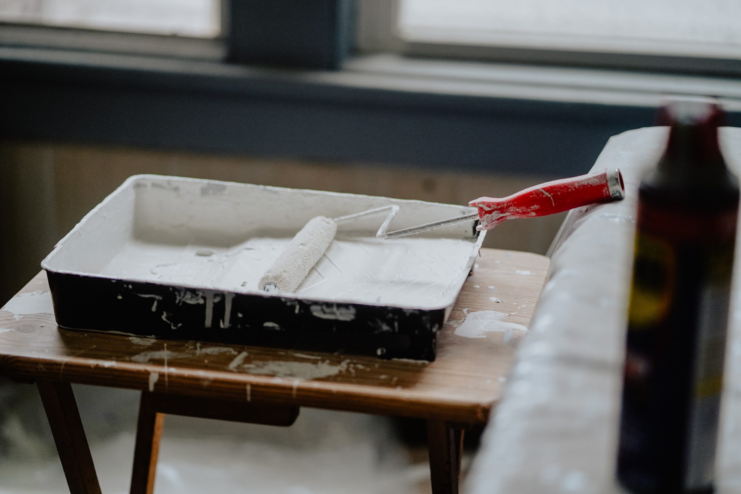 Paint Roller With Orange Handle In Paint Tray With White Paint On Wood Table