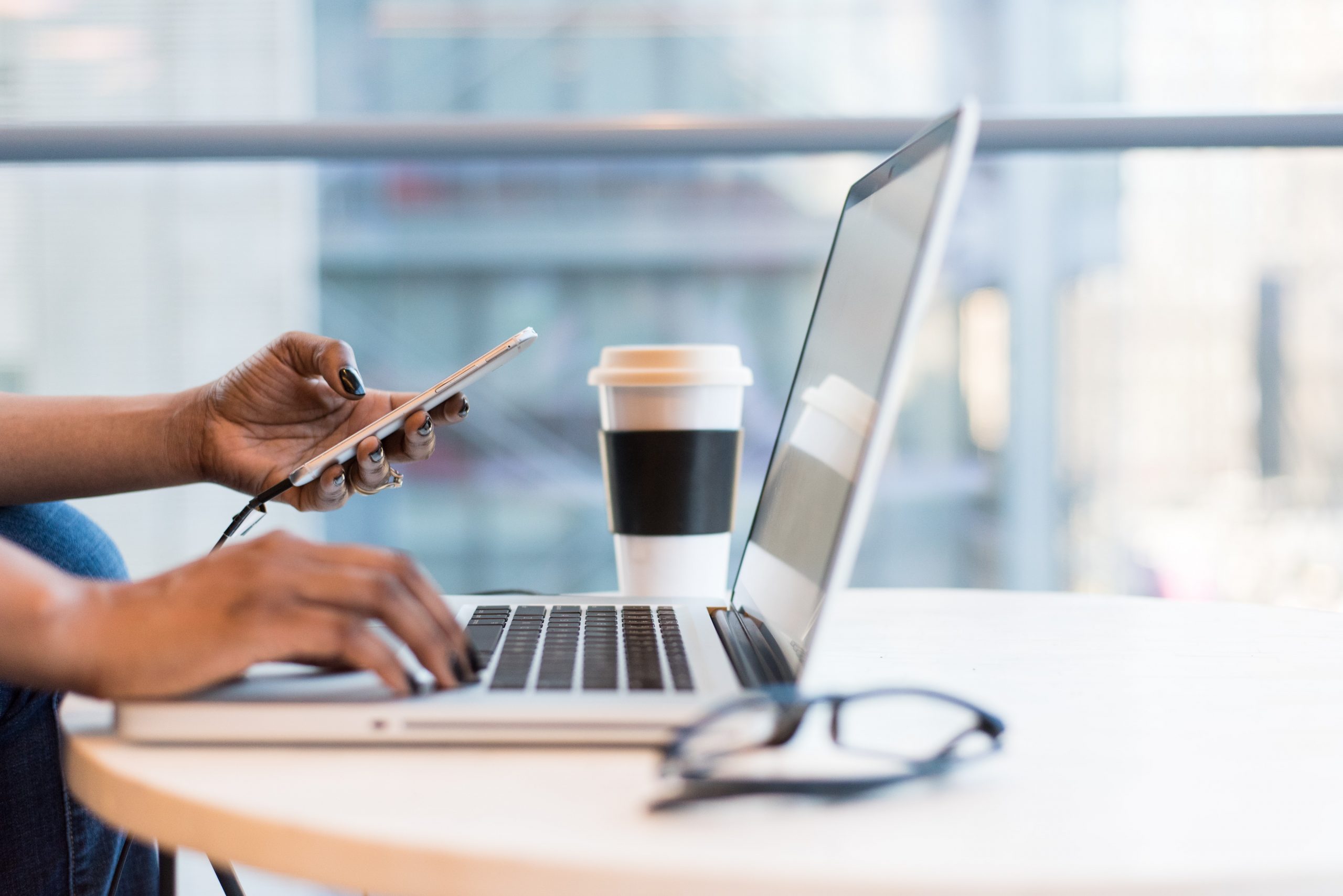 Women On Laptop With Phone And Glasses And Coffee Cup Sitting On Table